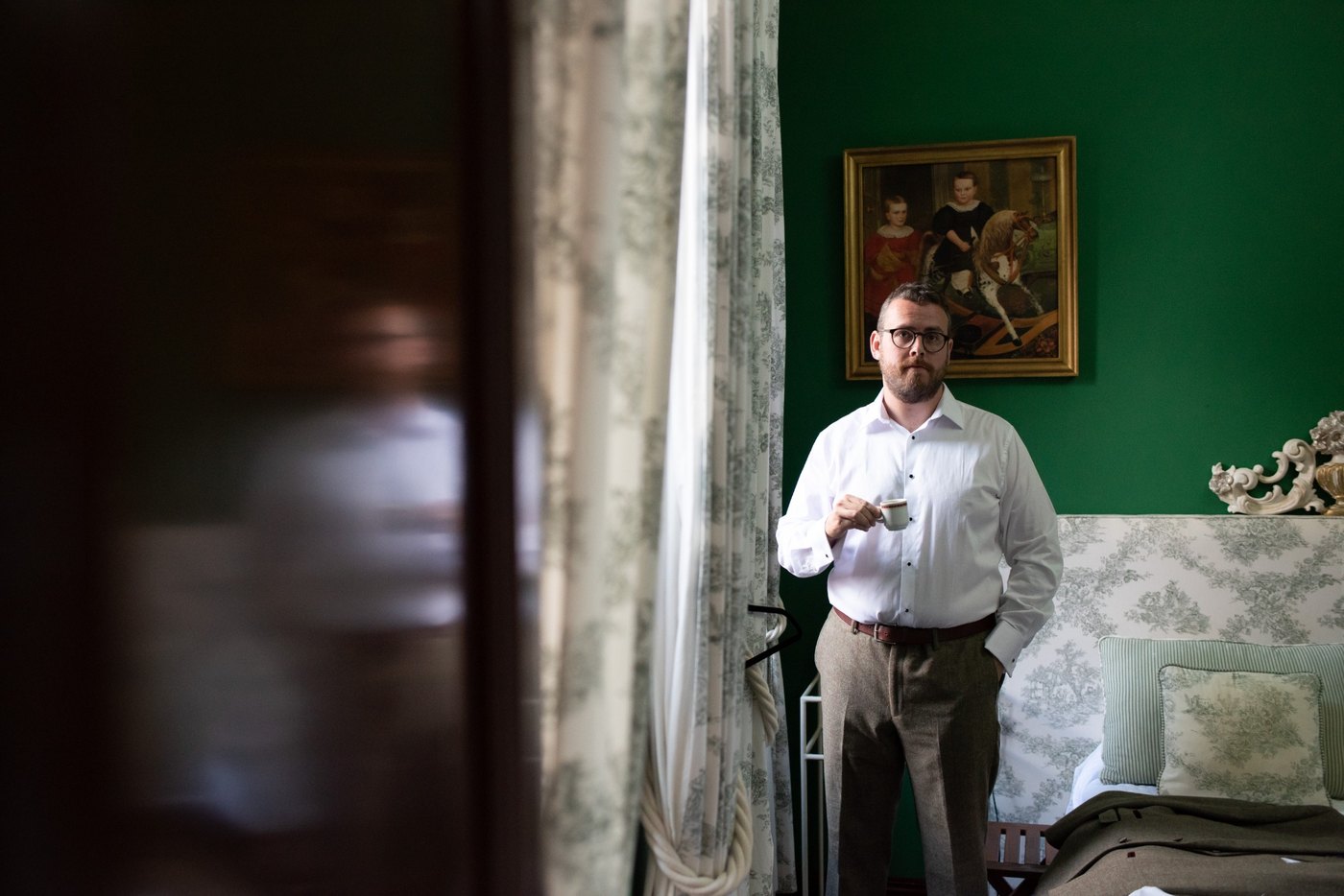 Tristan Hotham in round dark glasses with an espresso cup in a green-walled room